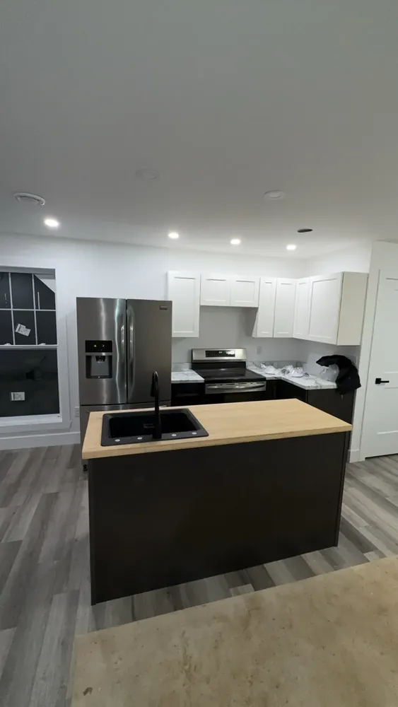 A Wildawbren-built kitchen with a butcher-block island and black sink, white shaker uppers, dark base cabinets, and stainless fridge and range