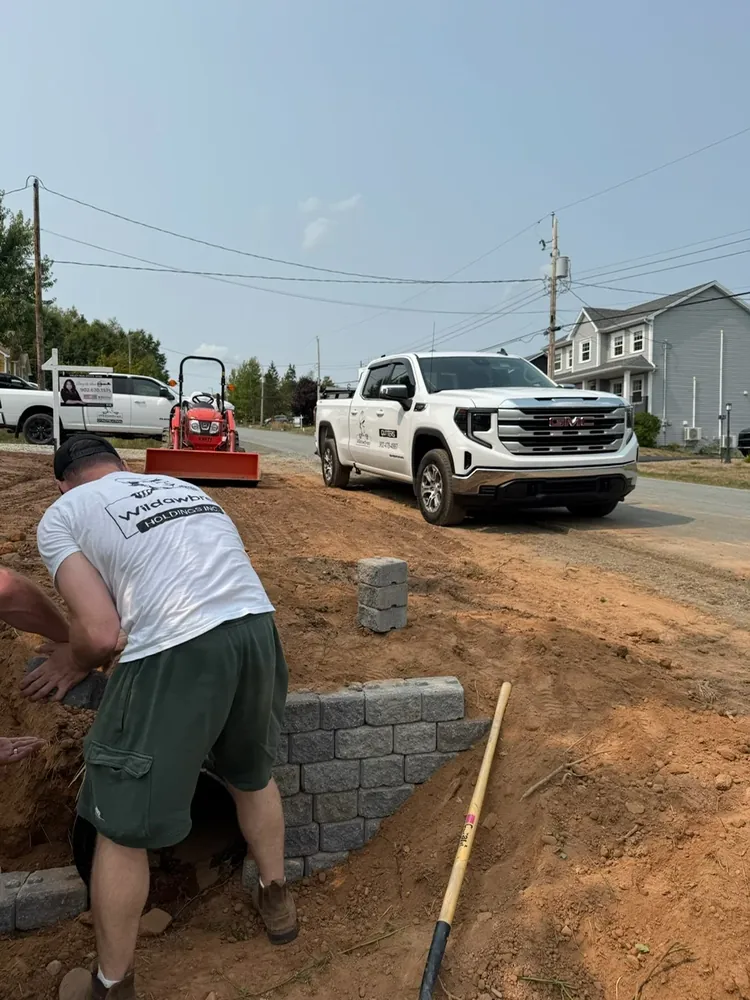 A Wildawbren crew member laying interlocking paver edging at street level, with a branded Wildawbren GMC pickup parked behind