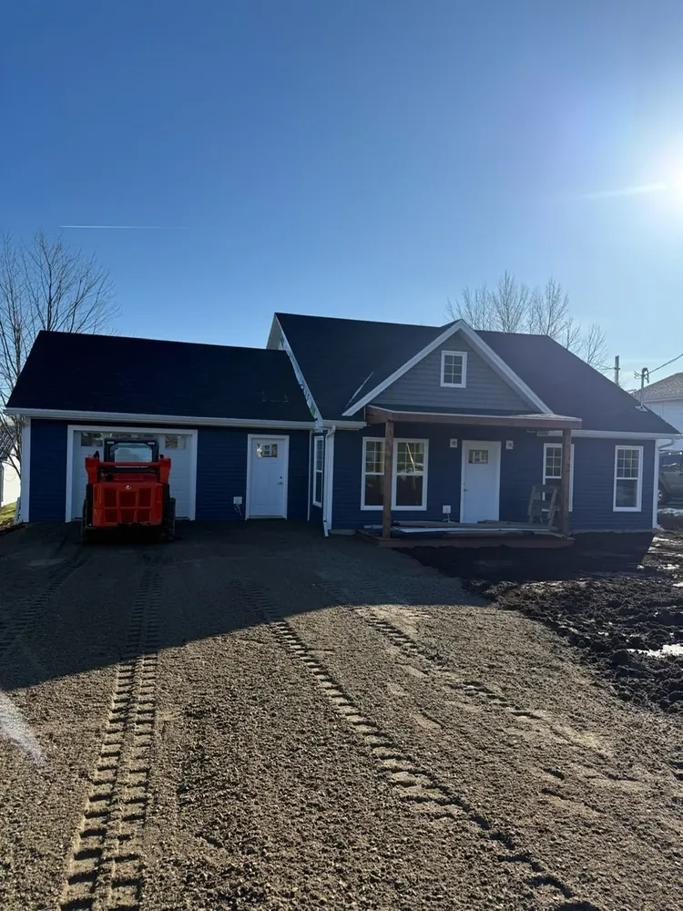 A Wildawbren finished blue ranch-style home with an attached garage and a freshly graded driveway, ready for handover