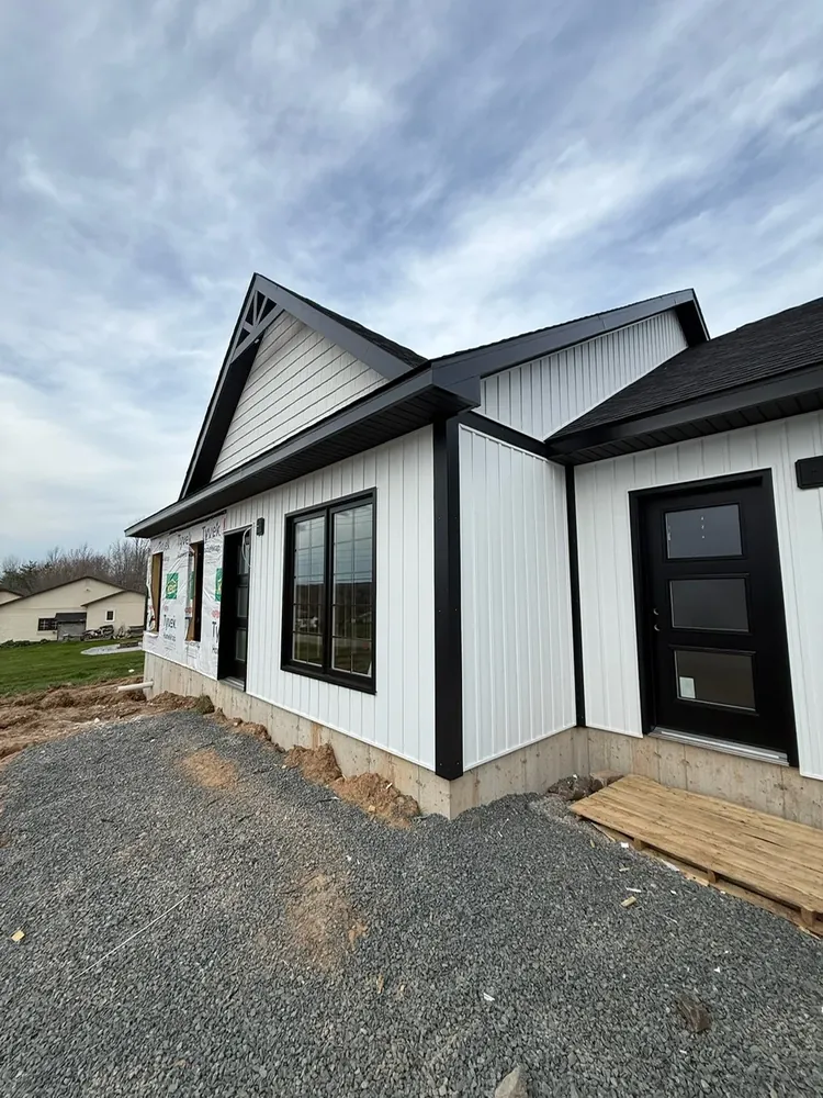A finished Wildawbren white board-and-batten home with crisp black seamless gutters running the length of the gable and porch rooflines